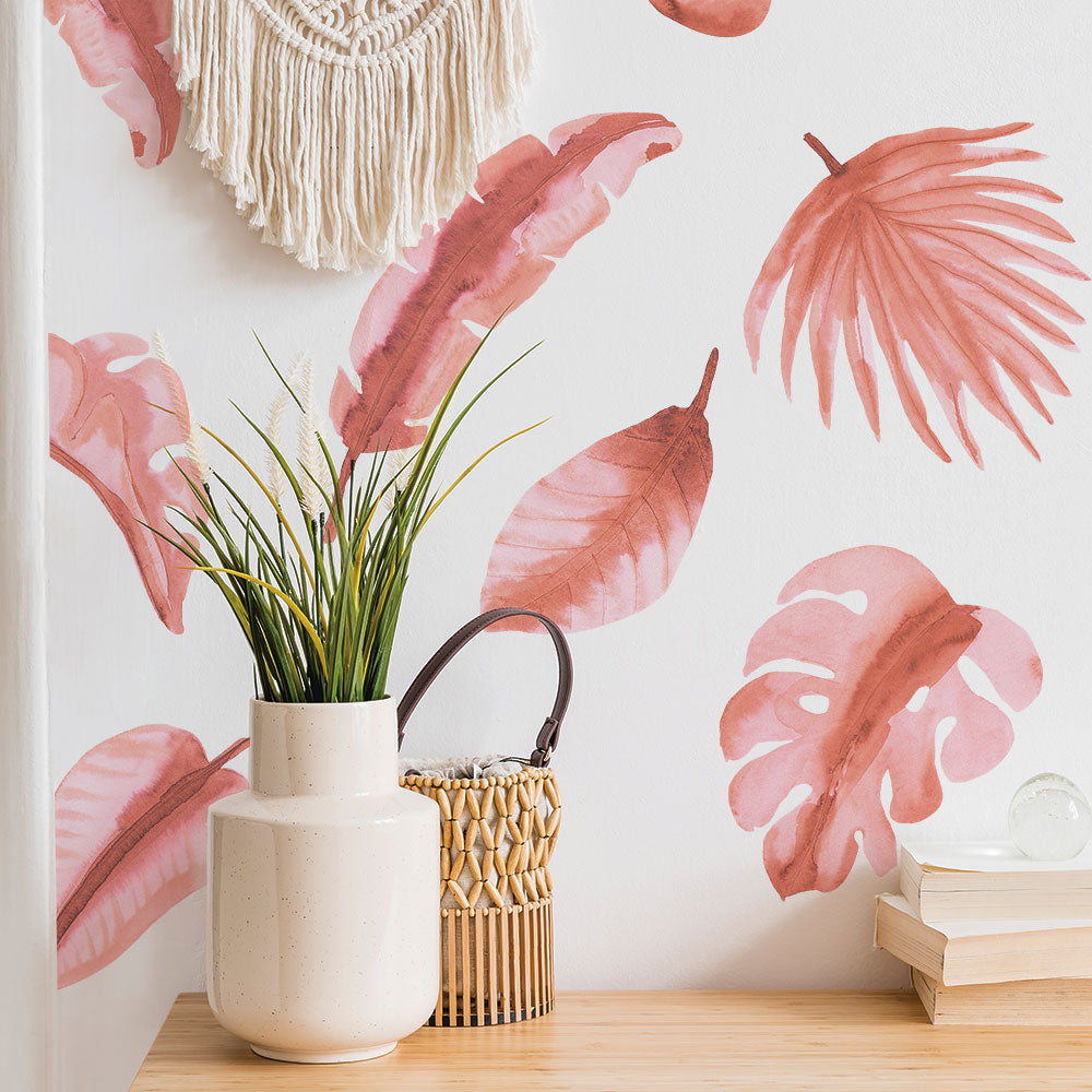 A white vase with a plant and several books in front of Tempaper's Watercolor Palm Leaf Wall Decals.