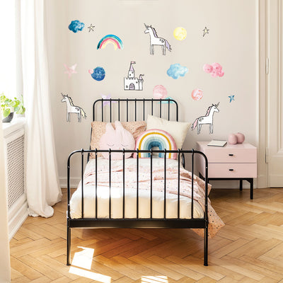 A kids bedroom with a bed and pink nightstand in front of Tempaper's Rainbows & Unicorns Temporary Wall Decals.