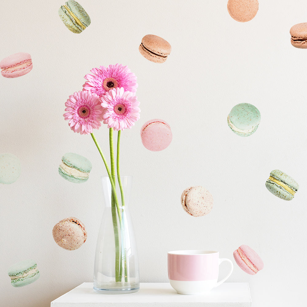A clear vase holding pink daisies next to a pink coffee mug with a wall decorated using Tempaper's French Macaron wall decals.
