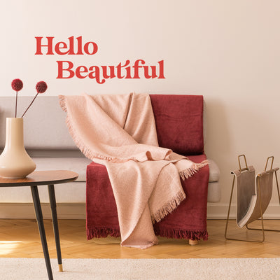 A living room with a couch, pink and red draped blankets, a magazine rack, a coffee table, and Tempaper's Hello Beautiful wall decal on the wall behind the couch.