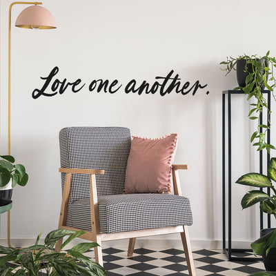 A room filled with green plants and a checkered black and white chair with Tempaper's Love One Another wall decal on the wall behind.