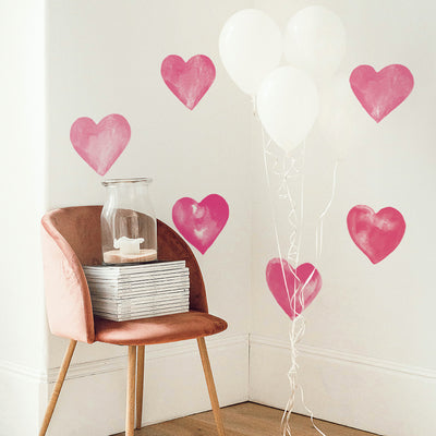 A corner with a chair holding magazines and a jar candle with Tempaper's Valentine's Day Heart wall decals on the wall behind. 