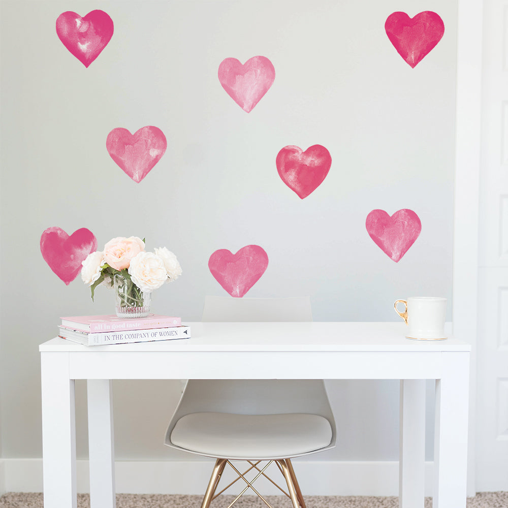 A wall filled with Tempaper's Valentine's Day Heart wall decals behind a white desk with a white desk chair, flowers, coffee mug, and a stack of books.