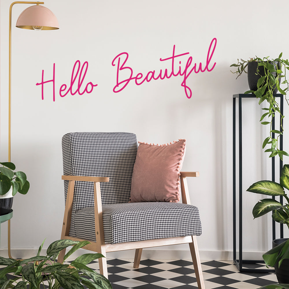 A black and white chair with pink pillow in a room filled with green plants and Tempaper's Hello Beautiful wall decal on the wall behind it.