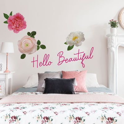 Tempaper's Hello Beautiful wall decals, along with our large flower wall decal, on the wall in a bedroom with a white bed and nightstand.