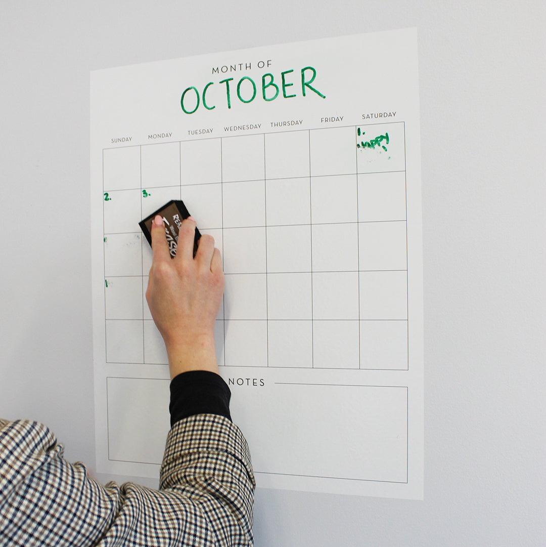 A person using an eraser on Tempaper's Dry Erase Monthly Calendar Wall Decal.