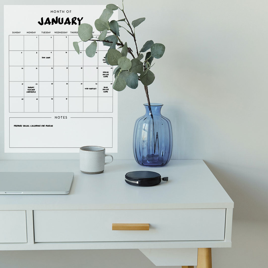 Tempaper's Dry Erase Monthly Calendar Wall Decal shown behind a plant.
