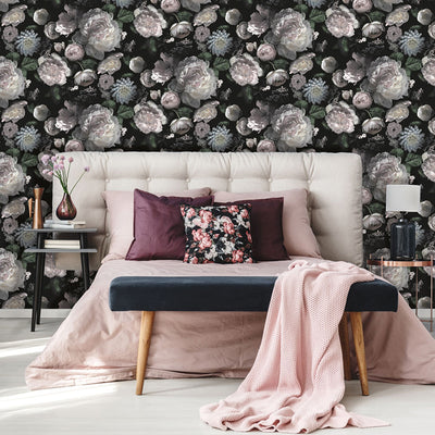 Moody floral peel-and-stick wallpaper from Tempaper on the wall of a bedroom with warm pink accents and a fabric headboard.