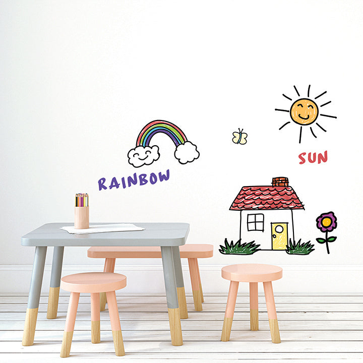 A child's art area with an art table and drawings of a rainbow, a sun, and a house on Tempaper's dry erase wallpaper.